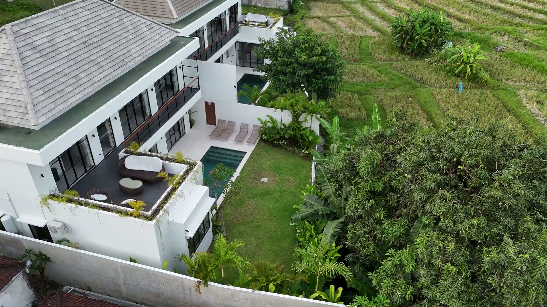Aerial orbit of Villa Rice by day, villas, pool, and rice field